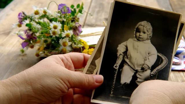 female hands holding paper envelope with old photographs, bouquet of wild flowers on table wooden table in garden, blurred natural background, concept of genealogy, memory of ancestors, family tree