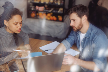 Fototapeta premium Hard-working man and woman sturtupers sitting in cafeteria and discussing project. Behind window.
