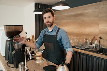 Smiling barista installs a container with coffee beans in the coffee machine and look at the camera