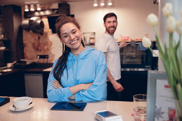 Obraz premium Beautiful stylish female barista standing at cafe counter and smiling. Cafeteria worker. Portrait.