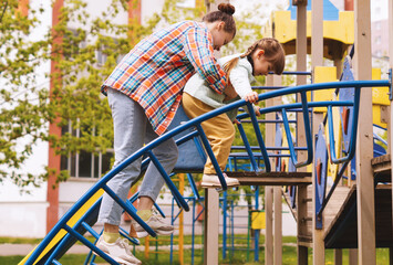 Sisters play on the playground on a summer day. A white girl in her 20s is playing in the park with a little girl.The older sister helps her younger sister up the stairs by supporting her.Nursing care