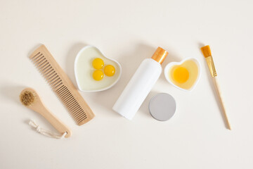 egg-based natural cosmetics concept, mock-up bottle, comb, brushes and raw egg in a small white heart-shaped bowl