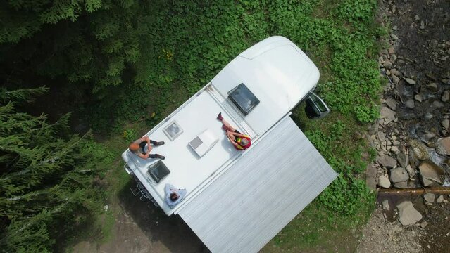 Caucasian Family Chilling Out on a Top of Their Camper Van Motorhome Enjoying Summer Vacation Sun. Rving Theme.