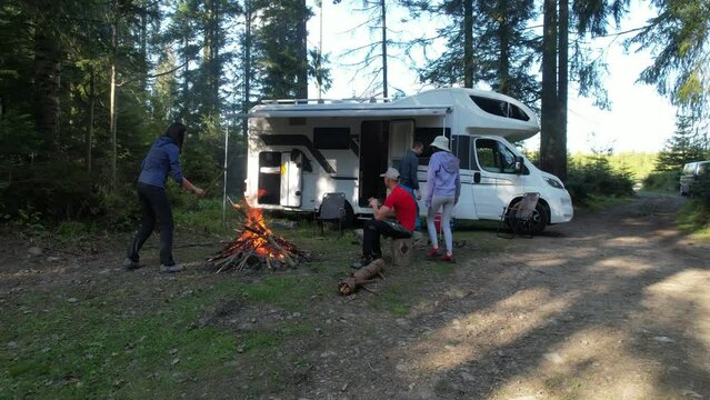 May 15, 2022 Babia Gora, Poland. RV Road Trip Vacation with Friends. Two Caucasian Couples Hanging Around Campfire Next to Their Motorhome Camper Van. Dry Camping in a Forest.
