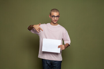 Happy student guy pointing at white empty paper banner on green background