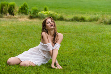 Attractive girl enjoys life, plays, wallows on a green fresh lawn in the rain. Wet hair and wet dress from watering the lawn