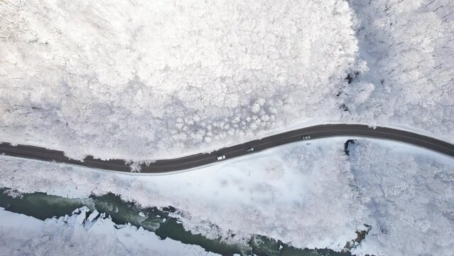 Aerial top down cinematic winter snow cowered country road, asphalt serpentine. Cars go traffic among forest.
