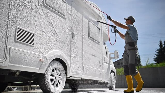 Caucasian Men in His 40s Pressure Washing Modern Class C Camper Van RV with Active Foam. Recreational Vehicle Maintenance.