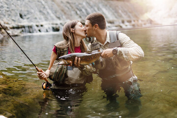 A young couple fishes on a fast mountain river and holds a trout in their hand. The concept of...