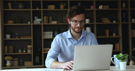 Young businessman employee in eyeglasses sit at desk in home office work use laptop, makes financial stats analysis, review online project revenue, take notes looks focused. Trading, workflow concept - Powered by Adobe