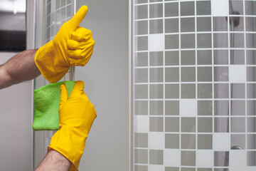 Man cleaning glass door in bathroom and showing thumb up closeup