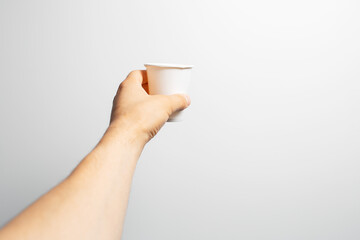 Close-up of male hand holding white paper cup of coffee takeaway, on grey.