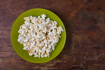 Green plate of salted popcorn on wooden table background. Top view, copy space
