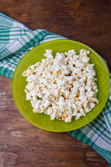 Green plate of salted popcorn on wooden table background with kitchen towel. Top view, copy space