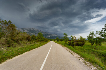 Fototapeta na wymiar Empty countryside road in valley. Landscape with dramatic sky. A storm is coming from the mountains.