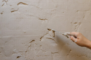 Male hands with spatula using putty for wall, builder making overhaul.