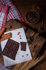 Broken bar of dark bitter chocolate with chilly pepper, red pea pepper, cinnamon flavour on paper,...