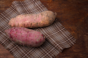 Orange, purple raw sweet potatoes, yam on wooden rustic table, fabric napkin. Farm harvest, organic vegetables, shop local vegan food