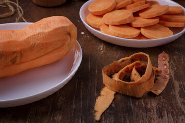 Orange raw sweet potato, skin, yam slices on plate, wooden rustic table. Farm harvest, organic vegetables, shop local, diet, nutrition