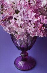 Beautiful lilac vintage faceted glass on a table with lilac flowers on a purple background