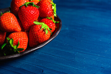 Fresh strawberries on a small black plate against a blue plaster design board.