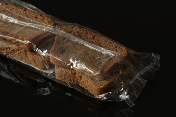 Dry bread wrapped in film on a black background. Bread rye, wheat.