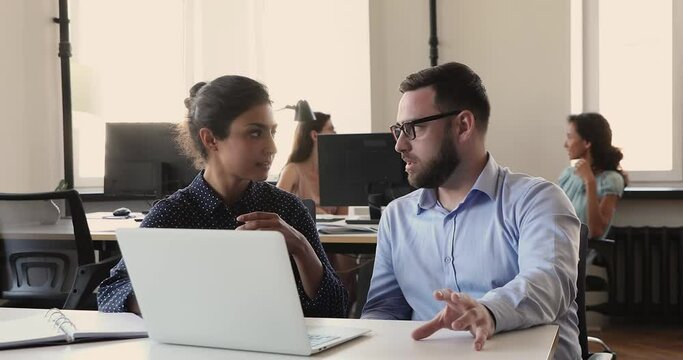 Focused businessman sales manager insurance agent consult young Indian woman client discuss deal details propose new solution. Two colleagues of different ethnicity gender talk brainstorm on workplace