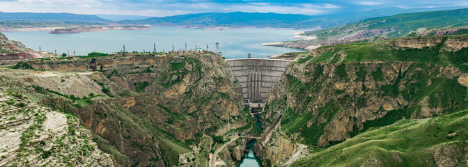 panorama with an arched hydroelectric dam and a reservoir in the mountain valley