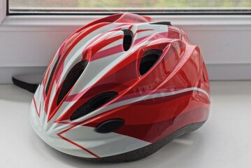 one large plastic red white bicycle helmet lies on a gray window sill by the window in the room
