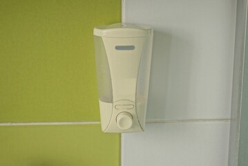 one gray plastic bottle with dispenser and liquid soap hanging on the wall on green white ceramic tiles in the bathroom