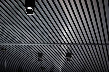 Bottom view of lath ceiling with spot lights. Abstract modern architecture or interior background in black and white with geometric structure. - obrazy, fototapety, plakaty