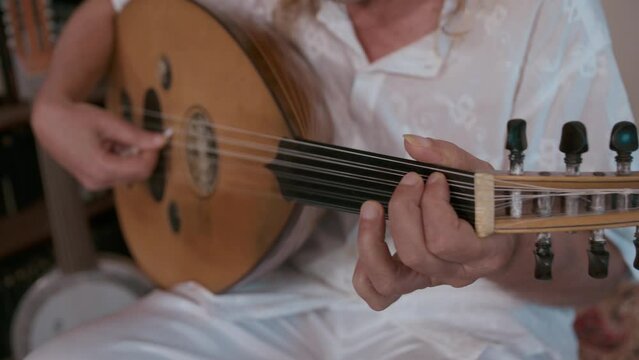 Elderly caucasian man in white shirt playing an oud. Close-up of hands with oriental string musical instrument. 4K