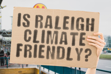 The question " Is Raleigh climate-friendly? " is on a banner in men's hands with blurred background. Support. Team. Activist. Urban. Sunset. Carbon. Ecology. Energy. New. Clean. Warming. Waste