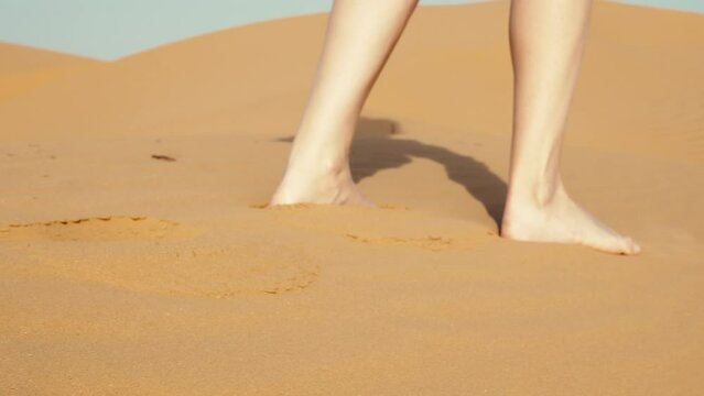 Female legs go on sand in desert. Feet of girl step, are drowning in dune. Faceless young woman walks with effort through hot barkhan. Wanderer, traveler moving with difficulty, surviving in heat