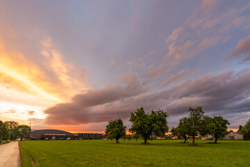 Abendrot nach abziehendem Gewitter. dramatischer Sonnenuntergang im Rheintal mit grüne Wiesen, Bäumen und farbige und graue Wolken, Dornbirn, Vorarlberg, Austria