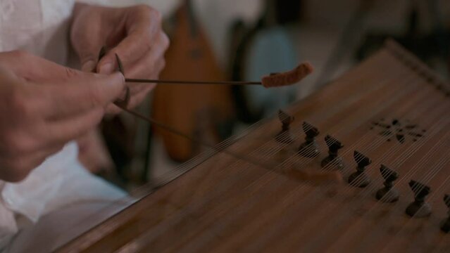 Elderly caucasian man playing traditional musical instrument of Middle East santur. Close-up of hands with small hammers and oriental string musical instrument.