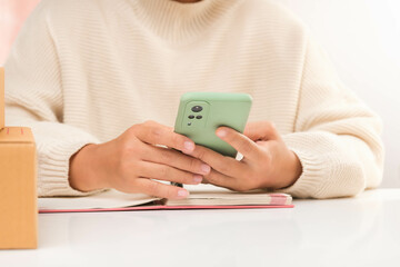 Young business woman working online shopping at her home with smart phone and online purchase shopping order and box packaging on table. Small Business Entrepreneur, SME or Freelance