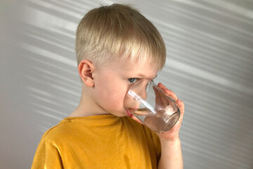 little boy in a yellow T-shirt drinks water