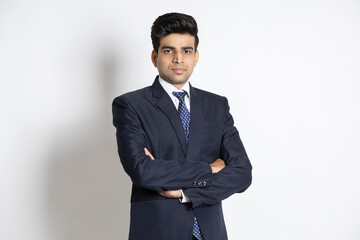 Obraz na płótnie Canvas Portrait of a confident young indian man wearing suit standing with his arms cross, isolated on white studio background.