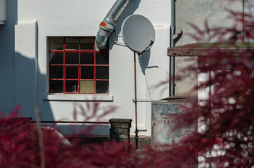 Satellite dish in the yard of a workshop and ventilation pipe through the mesh window - blurry reddish foreground
