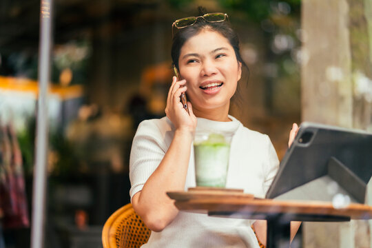 Smart Attractive Positive Asian Digital Nomad Female Wearing Casual Cloth Work Remote New Normal Lifestyle Hand Use Tablet Tele Conference Onlive Videocall Meeting Remote At Coffeeshop Cafe Restaurant