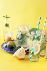 Useful cocktail of lemon slices, limes, mint leaves, in glass bottles on a yellow background, detox water, lemonade, natural drinks, home cooking