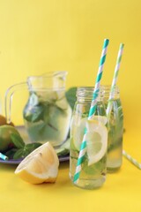 Useful cocktail of lemon slices, limes, mint leaves, in glass bottles on a yellow background, detox water, lemonade, natural drinks, home cooking