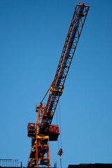 Silhouette of construction crane and unfinished residential building on blue sky background. Housing construction, apartment block in city. Vertical shot.