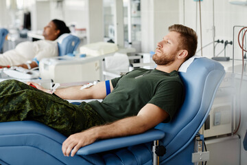 Side view portrait of military man donating blood while laying in chair at plasma donation center