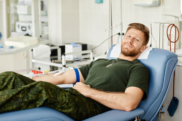 Portrait of military man giving blood while laying in chair at blood donation center and smiling at camera, copy space