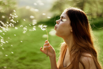 A female freelancer strolls carefree and happily in a green park and blows off a dandelion flower...