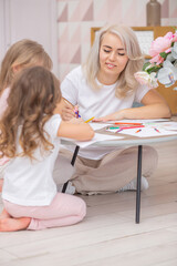 Smiling caucasian mom and two daughters draw together sitting on the floor