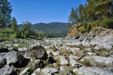 Fototapeta na wymiar A large cluster of stones of different sizes formed a stone river along the banks of majestic mountains.