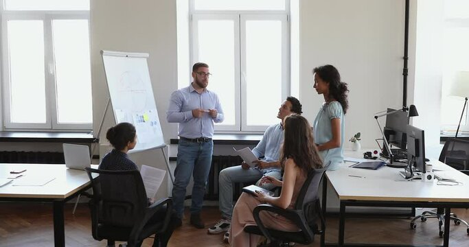 Businessman stand at whiteboard before multicultural audience give business class report on sales results explain strategy benefits. Young male startup developer present new project to investors group